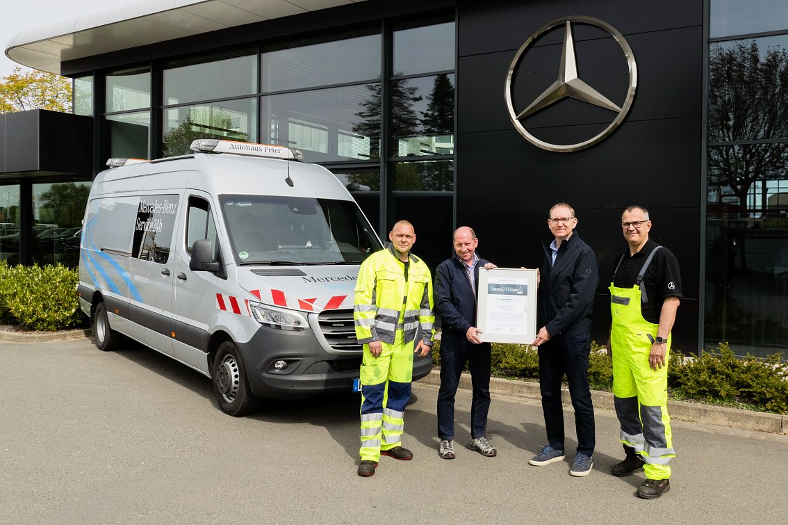 Vier M&auml;nner stehen vor einem Mercedes-Benz Service24h-Fahrzeug und halten die Auszeichnung Best of Service24h � 2025 von Daimler Truck. Im Hintergrund sind das Autohaus Peter und das Mercedes-Benz Logo zu sehen.