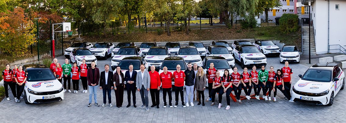 Spielerinnen des Th&uuml;ringer HC und Vertreter der Peter Gruppe posieren gemeinsam vor einer Flotte wei&szlig;er Opel-Fahrzeuge im THC-Design.