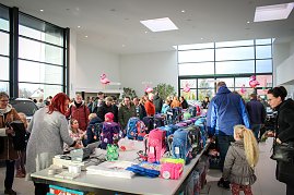 Viele Menschen, darunter Kinder mit Eltern, stehen an Tischen voller bunter Schulranzen im Autohaus. Rosa Flamingo-Dekorationen hängen von der Decke. Im Hintergrund sind Autos und große Fensterfronten sichtbar. (Foto: Autohaus Peter)