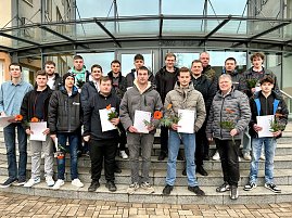 Abschlussklasse mit 16 Auszubildenden sowie einem Ausbildungsleiter und einem Berufsschullehrer auf der Treppe vor dem Eingangsbereich. Alle halten Zeugnisse und Blumen. (Foto: Autohaus Peter Gruppe)