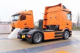 Zwei orangefarbene eActros 600 Lkw stehen nebeneinander an einer Ladestation. Im Hintergrund Bäume und ein Zaun. (Foto: ex animo MEDIA)