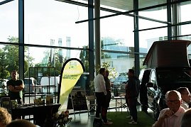 Ein Messestand mit gelb-grünem Banner Möbius – Grün macht glücklich!. Daneben ein schwarzer Mercedes-Camper mit hochgeklapptem Dach. Zwei Männer und weitere Personen unterhalten sich.