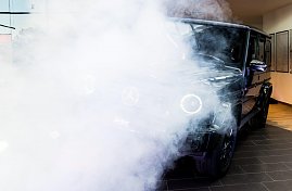 Eine schwarze Mercedes G-Klasse wird in Szene gesetzt. Dichter weißer Nebel und Scheinwerferlicht verdecken teilweise das Auto.