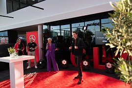 Ein Laufsteg-Moment: Ein junger Mann läuft über den roten Teppich, während Moderatorin Mandy Kossira im lila Hosenanzug mit Mikrofon spricht.