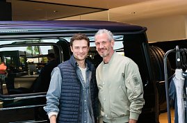 Zwei Männermodels stehen nebeneinander vor einem schwarzen Mercedes. Beide lächeln in die Kamera, einer trägt eine helle Bomberjacke, der andere eine dunkle Weste.