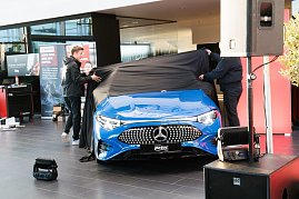 Ein blauer Mercedes CLA wird auf der Bühne präsentiert. Zwei Männer ziehen ein schwarzes Tuch von der Motorhaube.