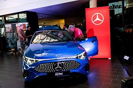 Ein blauer Mercedes CLA wird im Showroom präsentiert. Mehrere Besucher betrachten das Auto, während ein Mann in den Innenraum schaut.