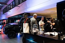 Ein Stand mit Mercedes-AMG-Merchandise: Vorne eine Schaufensterpuppe im Trainingsanzug, daneben Besucher, die Kleidung ansehen. Im Hintergrund ein schwarzer Mercedes-Geländewagen.