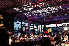 Viele Gäste sitzen an langen Tischen in der beleuchteten Eventhalle. An der Decke sind dekorative Lichtinstallationen angebracht.