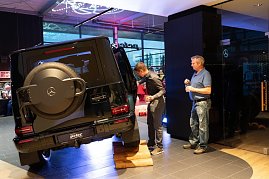 Ein schwarzer Mercedes-Geländewagen steht schräg auf einer Holzrampe, um seine Geländefähigkeit zu demonstrieren. Zwei Männer betrachten das Auto aus nächster Nähe.