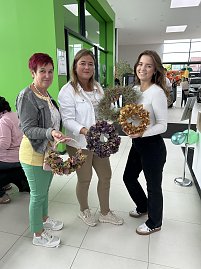 Drei Frauen stehen im Autohaus Autowelt Peter und halten selbstgemachte herbstliche Kränze in den Händen. Im Hintergrund sind weitere Gäste und grüne Luftballons zur Feier von 130 Jahren Škoda zu sehen.