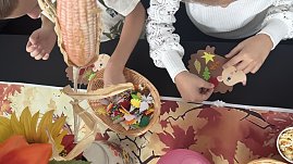 Kinder basteln im Autohaus Autowelt Peter herbstliche Figuren. Auf dem Tisch liegen bunte Papierblätter und ein Korb mit Bastelmaterial, während ein Igel aus Pappe mit Verzierungen gestaltet wird.