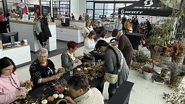 Besucherinnen und Besucher gestalten herbstliche Gestecke und Kränze an Basteltischen im Autohaus Autowelt Peter. Auf den Tischen liegen Kürbisse, Zweige und Blumen. Im Hintergrund sind weitere Stände und ein Fahrradbereich mit SCOTT-Zelt zu sehen.