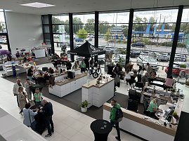 Blick von oben in den hellen Ausstellungsraum des Autohauses Autowelt Peter während der Feier zu 130 Jahren Škoda. Besucherinnen und Besucher sitzen an Tischen, basteln und stricken, andere informieren sich an Ständen, darunter ein SCOTT-Zelt mit Fahrrädern.