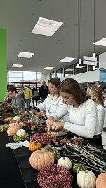 Besucherinnen gestalten an einem Basteltisch herbstliche Kränze mit Kürbissen, Beeren und Zweigen. Auf dem Tisch liegen bunte Naturmaterialien.