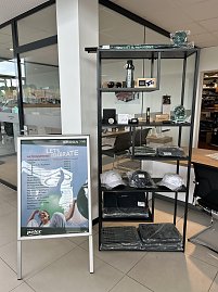 Vitrine mit Škoda-Merchandising-Artikeln wie Mützen, Flaschen und Accessoires im Autohaus Autowelt Peter. Daneben ein Aufsteller mit der Aufschrift ‚Let’s Celebrate – Aktionspreise‘.
