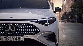 Das Bild zeigt einen weißen Mercedes-Benz CLA Shooting Brake, der auf einer breiten, nahezu leeren Stadtstraße fährt. Moderne Gebäude umgeben die Szene, das Licht wirkt weich und frühmorgendlich. Der Wagen ist seitlich zu sehen und vermittelt Dynamik sowie Eleganz.