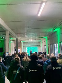 Blick von hinten auf die Räumlichkeit und die Gäste, mehrere Personen tragen schwarze Jacken mit Dekra Logo.