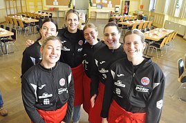 6 junge M&auml;dchen mit schwarzen Sportoberteilen und roten Sch&uuml;rzen l&auml;cheln in die Kamera.