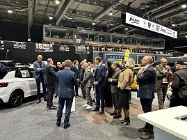 Mitarbeitergruppe auf der Automobilmesse stehen zwischen ausgestellten Autos und sprechen mit einem Messevertreter.