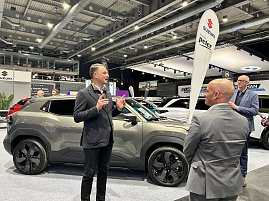 Andreas Peter erkl&auml;rt einen grauen SUV am Messestand, zwei Zuh&ouml;rer stehen davor. Im Hintergrund Suzuki-Banner und weitere Autos.