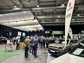 Besuchergruppe auf der Automobilmesse zwischen Messest&auml;nden und ausgestellten Autos, rechts ein Suzuki-Stand mit Banner.