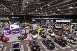 Panoramablick &uuml;ber eine Messehalle mit vielen ausgestellten Autos, Markenst&auml;nden und gro&szlig;en Werbebannern.