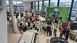 Gruppenfoto in einem Autohaus: Mitarbeitende und G&auml;ste stehen zwischen mehreren Fahrzeugen und zeigen Daumen hoch.