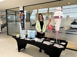 Frau steht hinter einem Infotisch mit Deko und Flyern, daneben gro&szlig;e Schult&uuml;te und Flamingo-Figur im Autohaus.