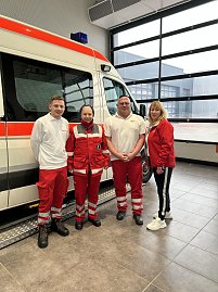 Vier Personen in DRK-Dienstkleidung stehen in einer Halle vor einem Rettungswagen.