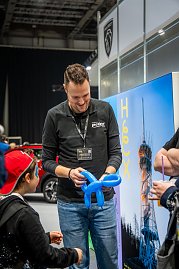 Mitarbeiter begeistert Kinder auf der Automesse mit Luftballons.