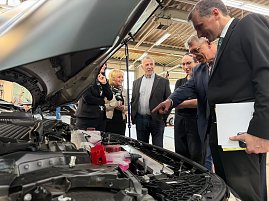 Teilnehmer des Pressegespr&auml;chs beim Rundgang in der Werkstatt an einem Fahrzeug bei offener Motorhaube.