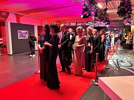 Elegant gekleidete G&auml;ste auf rotem Teppich im Eventbereich mit Beleuchtung.