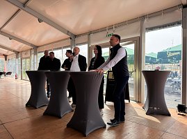 6 Personen stehen an mehreren Stehtischen, einer davon spricht ins Mikrofon.