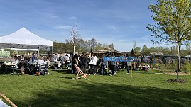 Ein Schild "Kreativwiese", dahinter Pavillons und mehrere Frauen an Biertischgarnituren.