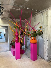 Kunstvoll inszenierte Blumenarrangements in knalligen Farben vor grauem Beton-Hintergrund