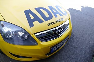 Vorderansicht eines gelben Opel-Fahrzeugs mit gro&szlig;em ADAC-Schriftzug auf der Motorhaube und der Webadresse www.adac.de. Das Auto steht auf Asphalt.