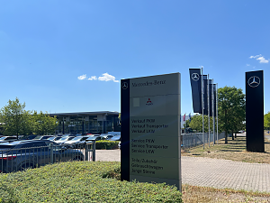 Großes Schild vor dem Mercedes-Benz Autohaus Peter in Dessau. Auf dem Schild stehen die Bereiche: Verkauf, Service, Teile/Zubehör, Gebrauchtwagen, Junge Sterne. Oben Logos von Mercedes-Benz und Fuso. Im Hintergrund das Autohaus.