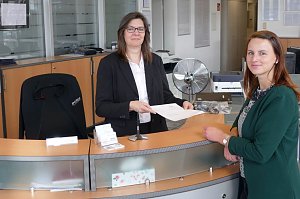 Zwei Frauen am Empfangstresen des Mercedes-Autohauses in Zerbst. Die Mitarbeiterin &uuml;bergibt ein Dokument an die Kundin, beide l&auml;cheln in die Kamera.