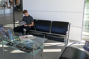 Kundenwartebereich im Mercedes-Benz Autohaus Bernburg, ein junger Mann sitzt auf einer schwarzen Ledersitzgruppe und liest eine Brosch&uuml;re, davor ein Glastisch mit Zeitschriften.