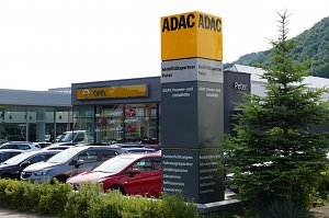 ADAC-Mobilit&auml;tspartner-Standort mit Autohaus Peter und Opel-Autohaus im Hintergrund. Vor dem Geb&auml;ude steht eine gro&szlig;e, auff&auml;llige ADAC-Stele mit gelb-schwarzer Beschriftung und Serviceangaben. Davor parken zahlreiche Fahrzeuge. Rechts im Bild ist ein Baum.