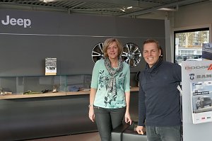 Christel Lauterbach und Danny Kindervater vom Jeep-Team stehen lächelnd vor dem Wartebereich im Jeep-Autohaus; im Hintergrund Wand mit Jeep-Logo und Felgen.