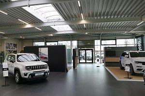 Innenraum eines modernen Jeep-Autohauses mit zwei ausgestellten weißen SUV-Modellen, großen Glasfronten und heller, offener Architektur.