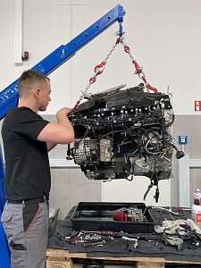 Mechaniker &uuml;berpr&uuml;ft einen mit einem Kran angehobenen Motorblock in der Mercedes-Werkstatt.