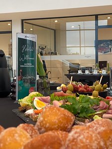 Nahaufnahme eines Buffets mit belegten Brötchen, Obst, Gemüse und Käseplatten. Daneben steht ein Begrüßungsaufsteller zum Škoda Unternehmerfrühstück.