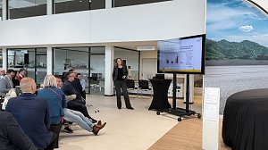 Teilnehmende verfolgen einen Vortrag im hellen Škoda-Ausstellungsraum. Ein Bildschirm zeigt Diagramme, im Vordergrund Frühstückstische.