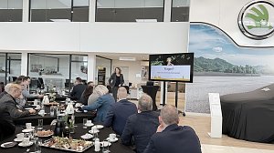 Eine Rednerin steht im Škoda-Ausstellungsraum vor einem Bildschirm mit der Folie Fragen? Vielen Dank für Ihre Aufmerksamkeit!. Gäste sitzen an gedeckten Frühstückstischen und hören zu.