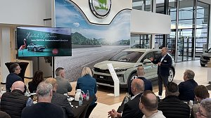 Ein Referent spricht vor einem Publikum, während der neue Škoda Elroq im Showroom präsentiert wird. Links auf einem Bildschirm die Begrüßungsfolie Herzlich Willkommen zum ŠKODA Unternehmerfrühstück.