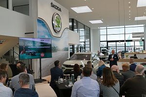 Viele Gäste sitzen an Tischen im Showroom, während ein Referent den neuen Škoda Elroq präsentiert. Links der Begrüßungsbildschirm, rechts der Empfangsbereich des Autohauses.
