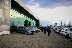 Das Škoda Autohaus mit moderner Glasfassade. Vor dem Gebäude stehen mehrere neue Škoda-Fahrzeuge, Besucher gehen zwischen den Autos hindurch.